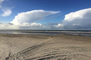 Ein Strand mit weitem Sandbereich, wenigen Personen und einem klaren Himmel mit Wolken.