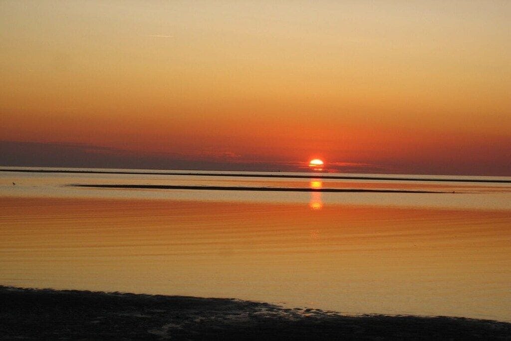 Auringonlasku tyynen vesistön yllä, horisontti on selkeästi näkyvissä.