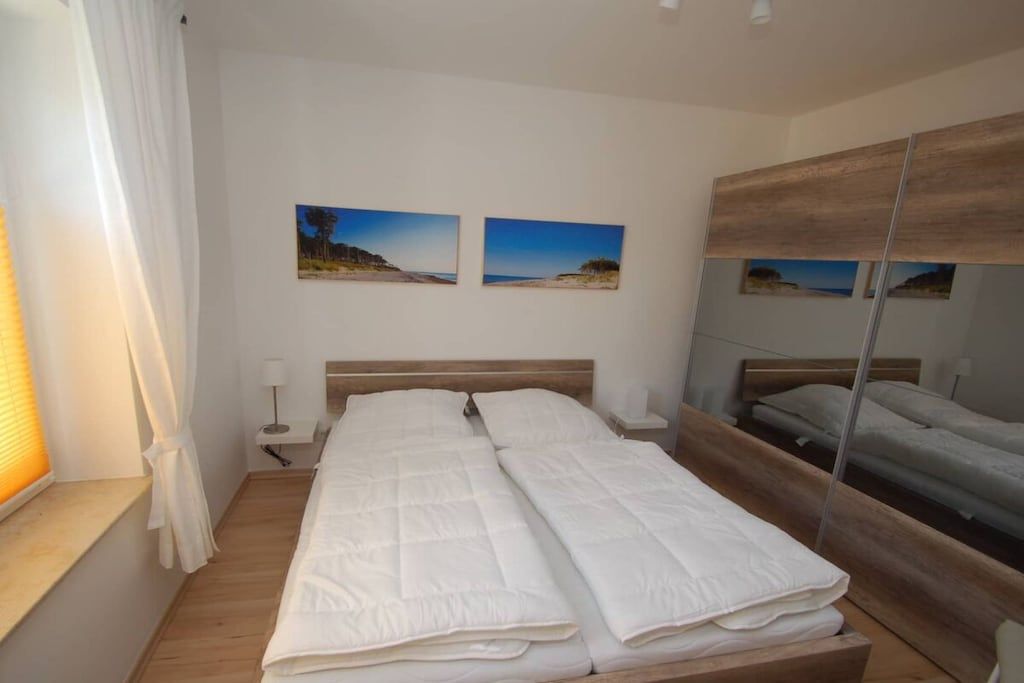 A bedroom with a large bed, two wall-mounted pictures, a bedside table with a lamp, and a mirror.