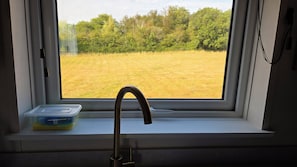 Una ventana con vista a un campo y árboles, un lavamanos y un jabonera.