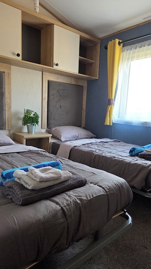 Habitación de hotel con dos camas, una mesita de noche con una planta y una ventana con cortinas.