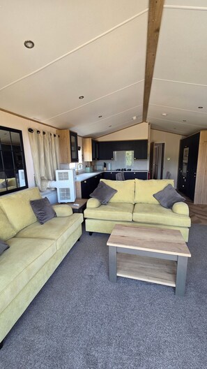 A modern living room with a sofa set, a coffee table, and a kitchen area in the background. - Killymoon Lodge – Luxury Adults-Only Escape with Private Hot Tub (Newport)