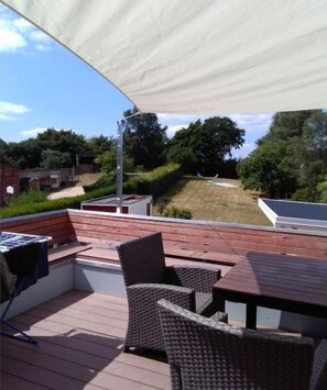A covered outdoor seating area with wicker furniture and a table, overlooking a garden and a building. - Holiday apartment with 3 bedrooms (Fargau-Pratjau)
