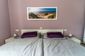 A double bed with two pillows, a nightstand with a lamp, and a framed picture of a beach scene on the wall. - Holiday apartment with 1 bedroom (Zingst)