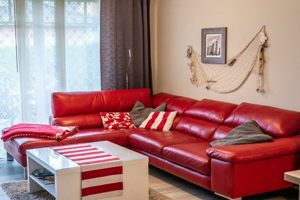 Um sofá de couro vermelho com almofadas listradas, uma mesa de centro de vidro e uma rede pendurada na parede.