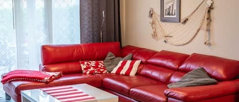 En rød lædersofa med stribede puder, et glasbord og en hængekøje på væggen.