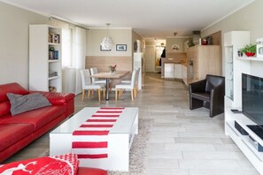 A modern living room with a red sofa, a white coffee table, and a dining area with a white table and chairs. - Holiday apartment with 1 bedroom (Zingst)