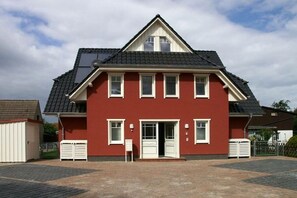 A two-story house with a red facade, white trim, and a dark roof. - Holiday apartment with 1 bedroom (Zingst)
