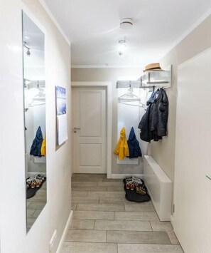 A narrow hallway with a door at the end, a mirror on the left, and a coat rack with jackets on the right. - Holiday apartment with 1 bedroom (Zingst)