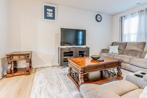 A living room with a flat-screen TV, a wooden coffee table, a sofa, and a patterned rug. - Capstan Terrace - Fully Furnished 3-Story Townhome with Garage and Private Patio in Charlotte (Charlotte)