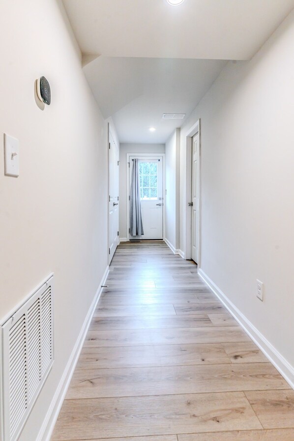 A hallway with white walls, a wooden floor, and a door at the end. - Capstan Terrace - Fully Furnished 3-Story Townhome with Garage and Private Patio in Charlotte (Charlotte)