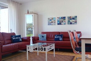 Ein Wohnzimmer mit einem roten Sofa, einem Glastisch und einer Wand mit maritimer Kunst.
