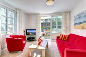 A living room with a red sofa, a coffee table, and a TV. There are large windows and a view of greenery outside. - Residence on Balmer Lake RadundMeer (Balm\/Usedom)
