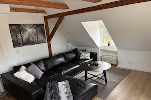 Ein modernes Wohnzimmer mit einer schwarzen Ledersofa, einem runden Couchtisch und einem großen Fenster, das für natürliches Licht sorgt.