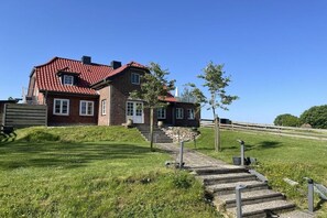 Ein zweistöckiges Haus mit rotem Ziegeldach, einer Steintreppe, die zum Eingang führt, und einem Rasen.
