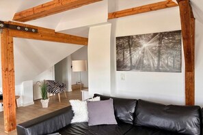 A modern living room with a black leather sofa, a zebra-patterned chair, a potted plant, and a large forest-themed painting on the wall. - "Loft on the fjord at the Schlei" (Borgwedel)
