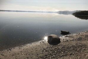 Ein ruhiger See mit klarer Spiegelung, felsigem Ufer und einer entfernten Baumgrenze.