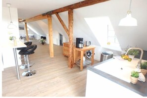 A modern kitchen with a wooden ceiling, a dining area with a table and chairs, and a kitchen island with a sink and potted plants. - "Loft on the fjord at the Schlei" (Borgwedel)
