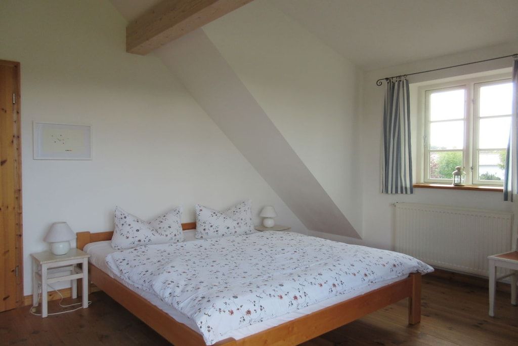 A bedroom with a wooden bed, a nightstand, a window with curtains, and a radiator.