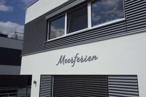 Un edificio con el nombre 'Meerfieren' en la fachada, que presenta listones horizontales en la parte superior y un amplio ventanal.