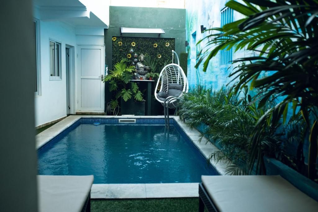 Piscina com cadeira suspensa, cercada por plantas e uma parede com estátua de Buda.