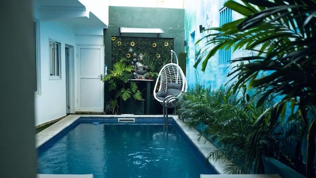 A swimming pool with a hanging chair, surrounded by plants and a wall with a Buddha statue. - Alojamento Local Onzo Yamy (Luanda)