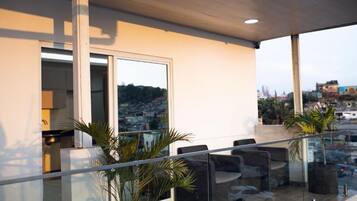 A modern balcony with glass railings, seating, and potted plants.