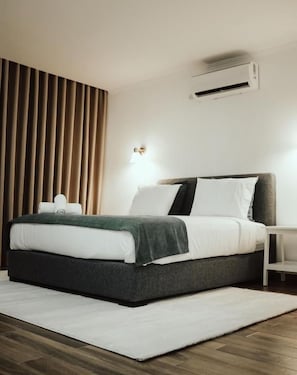 Et moderne hotelværelse med en seng, et natbord, en vægmonteret aircondition og et vindue med persienner.