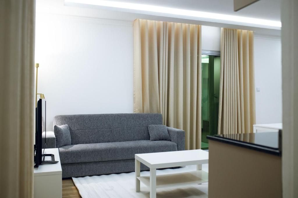 Uma sala de estar moderna com um sofá cinzento, uma mesa de centro branca e cortinas bege.
