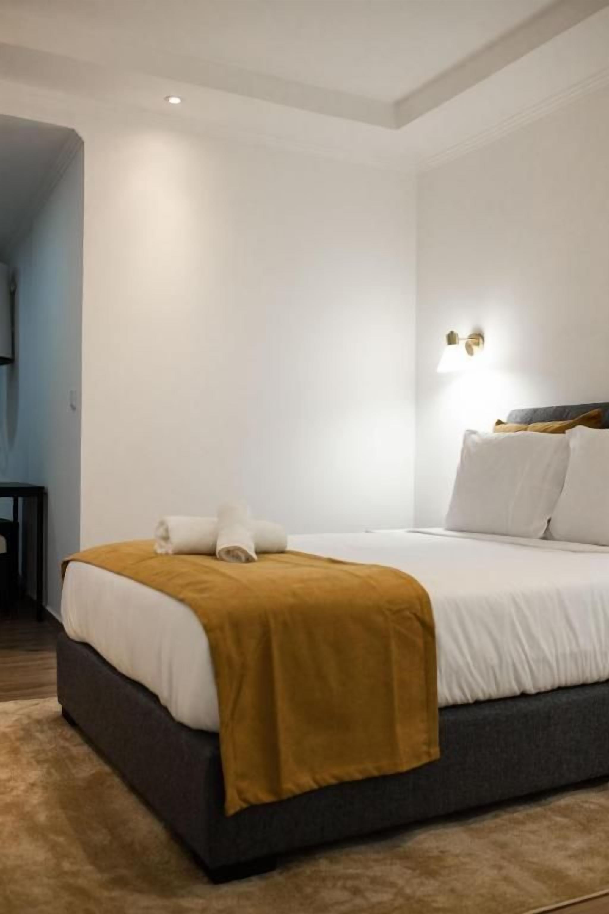 Una habitación de hotel con una cama, una mesita de noche y una lámpara de pared.