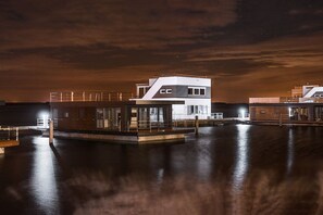 En fastighet vid vattnet med en modern tvåvåningsbyggnad, en brygga och fri utsikt över vattnet.