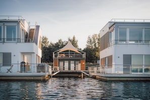 Ein modernes Ufergrundstück mit einem zentralen Gebäude mit Satteldach, flankiert von zwei weißen Gebäuden mit Balkonen und großen Fenstern.