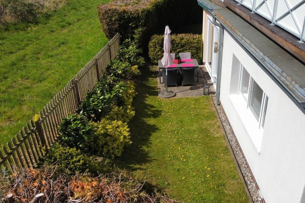 Un jardín cercado con una mesa y sillas, un edificio blanco y un seto.