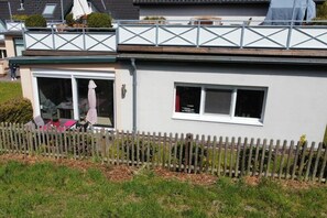 Ein Wohngebäude mit überdachter Terrasse, einem eingezäunten Garten und einem sichtbaren Fenster.