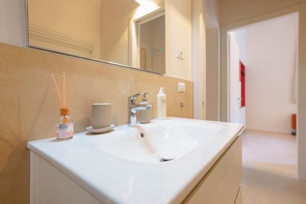 Une salle de bain d’hôtel avec un lavabo blanc, un miroir et un flacon de diffuseur de parfum à bâtonnets.