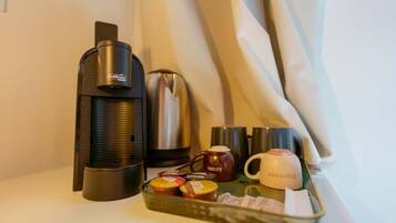 Una cafetera, una olla de acero inoxidable, una taza y una bandeja con recipientes sobre una mesa.