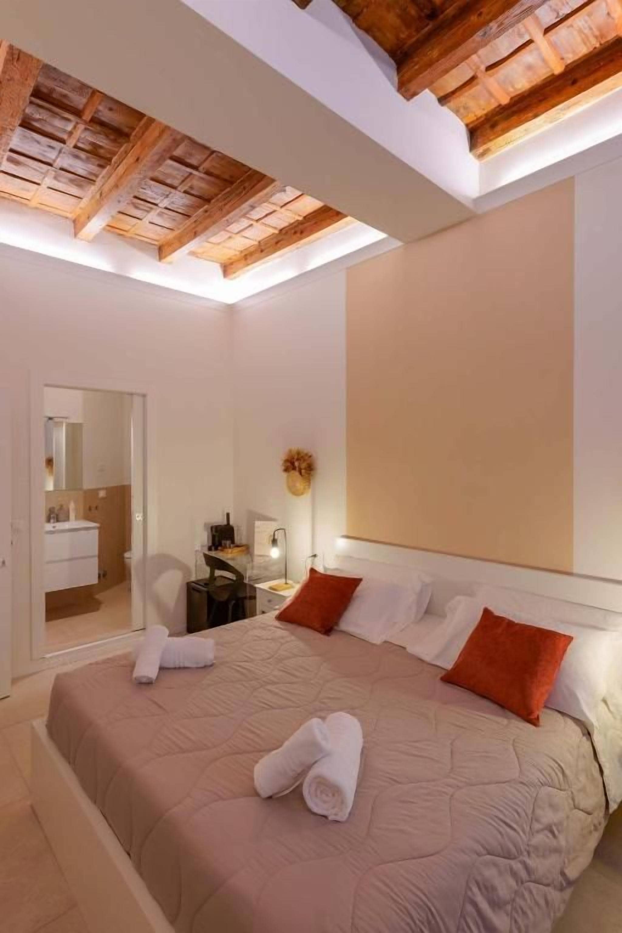 Ein Schlafzimmer mit einem großen Bett, einer Holzbalkendecke, einem Nachttisch mit Lampe und einem Spiegel.