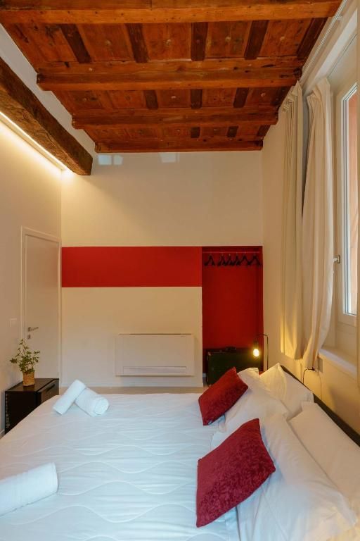 Une chambre d’hôtel avec un plafond en bois, un lit avec une literie blanche et des oreillers rouges, un mur d’accent rouge et une fenêtre avec des rideaux.