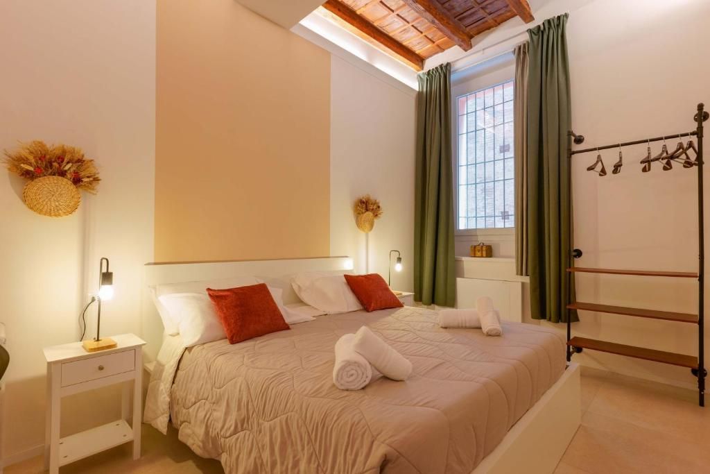Un dormitorio con cama, mesitas de noche, una ventana con cortinas y un perchero con ropa colgada.