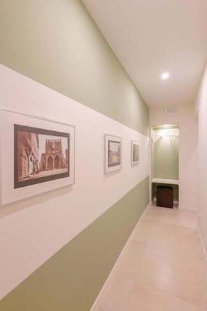 Un couloir avec des tableaux encadrés accrochés au mur, une poubelle et un luminaire.
