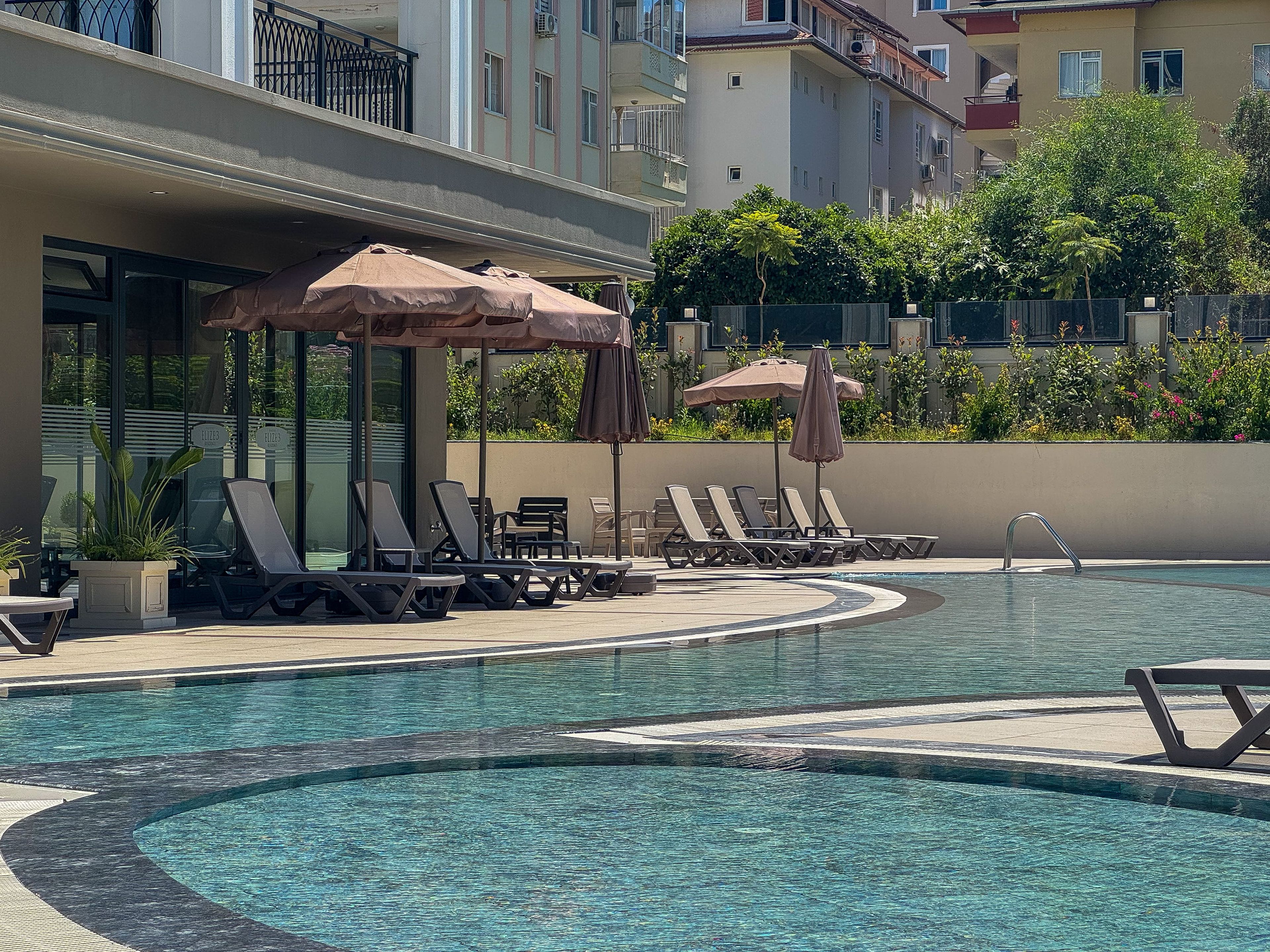 A swimming pool with lounge chairs and umbrellas, surrounded by a building with balconies.