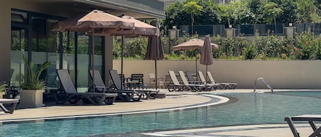 A swimming pool with lounge chairs and umbrellas, surrounded by a building with balconies.