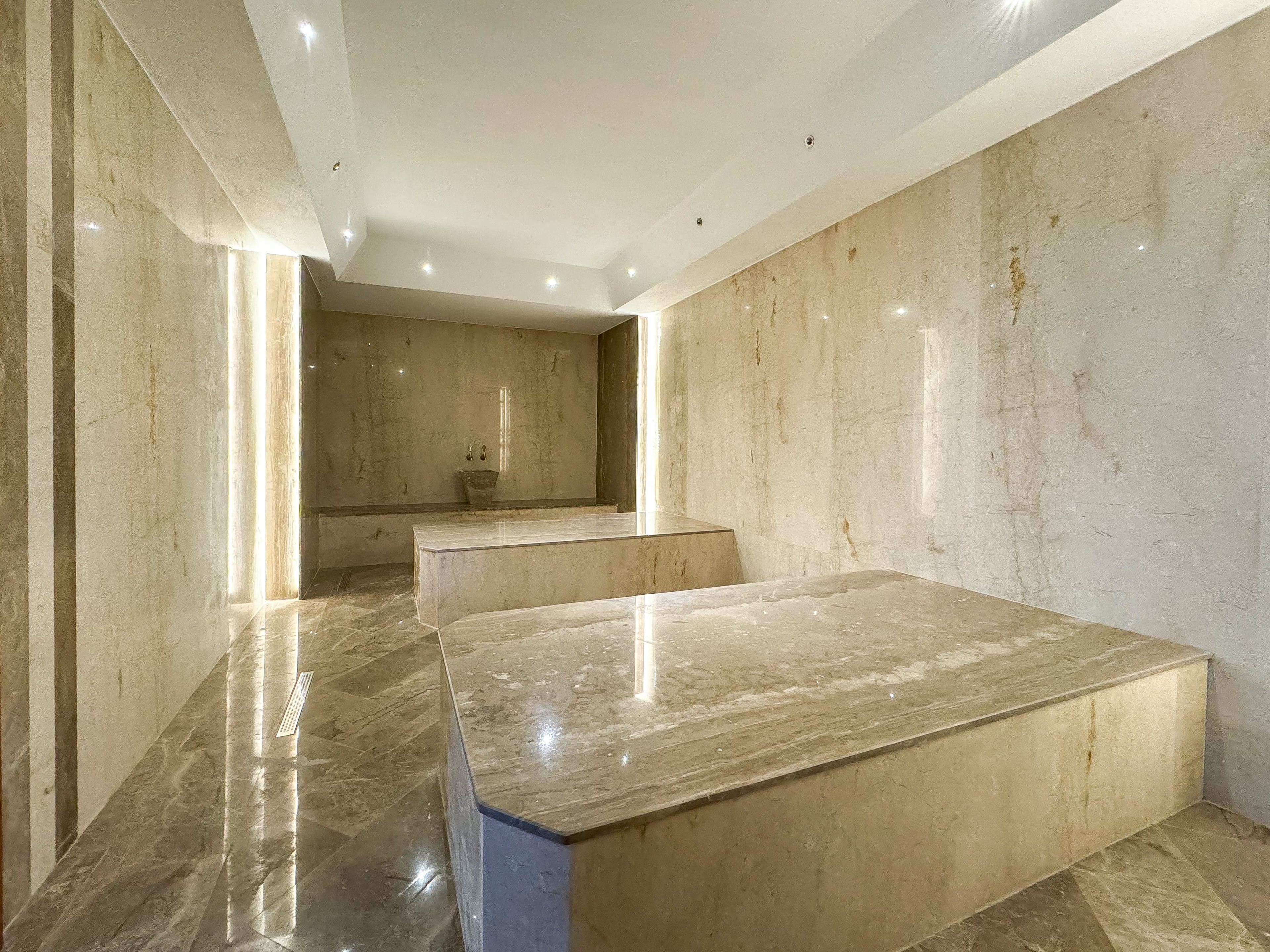 Un baño moderno con pisos y paredes de mármol, un espejo grande y una bañera.