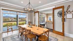 Uma sala de jantar com mesa e cadeiras de madeira, um candelabro e vista para o exterior.