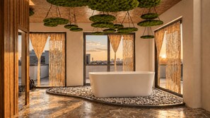 Ein modernes Badezimmer mit einer freistehenden Badewanne, Bambusvorhängen und Blick auf die Stadt.
