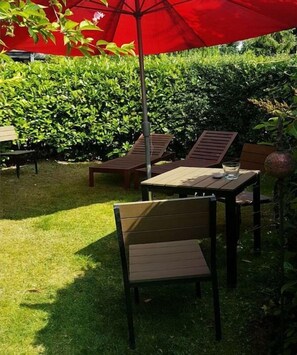 An outdoor seating area with a table and chairs under a red umbrella, surrounded by greenery. - "House on Lake Selent" (Köhn \/ Pülsen)