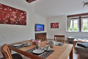 A dining area with a wooden table set for two, a television on the wall, and a window with curtains. - Holiday apartment with 3 bedrooms (Börgerende)