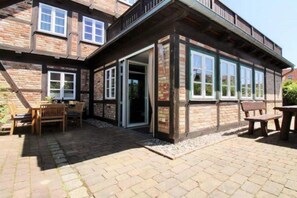 A two-story building with a patio area featuring outdoor seating and a door leading to the interior. - Holiday apartment with 3 bedrooms (Börgerende)