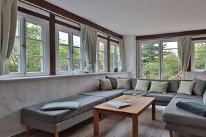 A modern living room with a large sectional sofa, a wooden coffee table, and large windows with curtains. - Holiday apartment with 3 bedrooms (Börgerende)