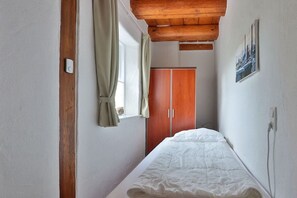 A bedroom with a bed, wooden ceiling beams, a wardrobe, and a window with curtains. - Holiday apartment with 3 bedrooms (Börgerende)